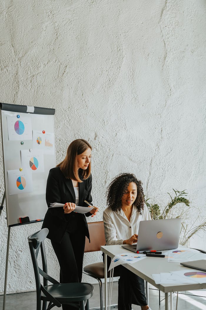 gallery-05 Two businesswomen analyzing graphs on a whiteboard during a meeting.
